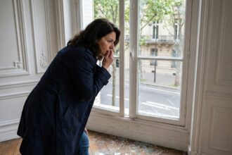 Femme parisienne regardant une vitre brisee dans son appartement