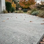 Terrasse extérieure en béton brut brossé avec joints de dilatation visibles et bordure en bois dans un jardin résidentiel en automne